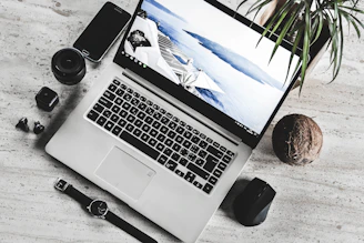 A cozy workspace featuring a laptop displaying dazzliy.online, surrounded by a smartwatch, wireless earbuds, and a portable power bank.