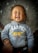 A young child with closed eyes is smiling widely, wearing a gray hoodie with the word 'CHAMPION' and some letters and designs in yellow and red. The child appears to be held by an adult whose hand is visible on the left side of the image, and they are set against a textured background.