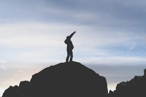 A climber reaching the summit at sunset, symbolizing achievement and connection.