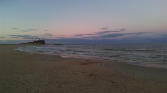 A serene Atlantic coastline at sunset with waves gently lapping against rocky shores and a lighthouse in the distance.