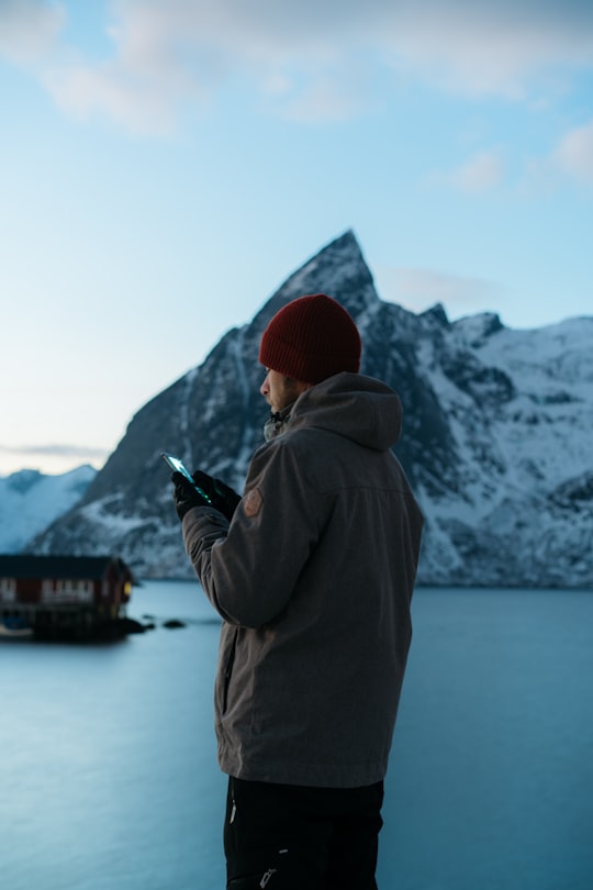 man using smartphone near mountain covered with snow in Hamnøy Norway