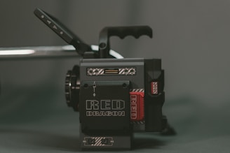 A professional-grade cinema camera with a blocky, industrial design featuring black and grey colors. The prominent branding 'RED DRAGON' is visible, and there are various buttons and handles on the camera.