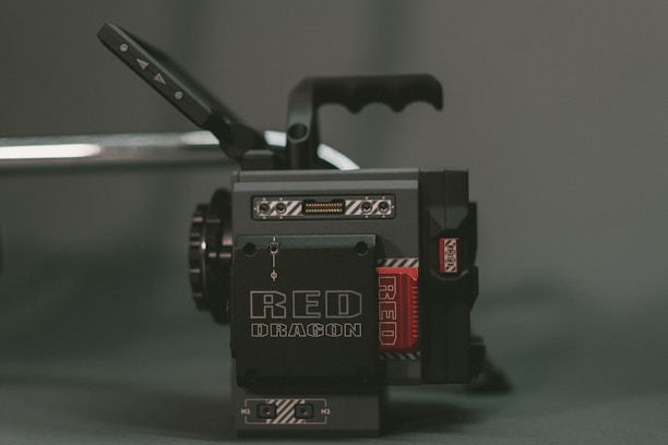 A professional-grade cinema camera with a blocky, industrial design featuring black and grey colors. The prominent branding 'RED DRAGON' is visible, and there are various buttons and handles on the camera.