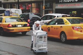 man pushing gray bus cart on road near two yellow taxi cabs
