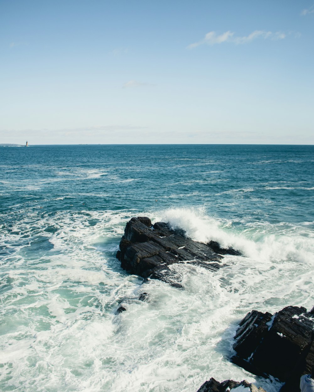 昼間の青空の下、岩に打ち寄せる海の波