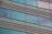 Glass windows of a modern building with horizontal metal frames and reflective surfaces. Some windows show vertical blinds partially drawn, allowing a view of interior silhouettes.