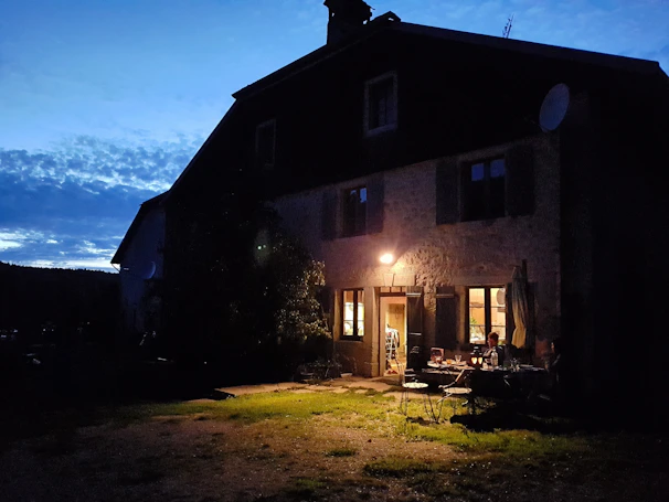 Exterior view of the stone house at dusk with soft lighting highlighting the texture and natural tones of the materials.