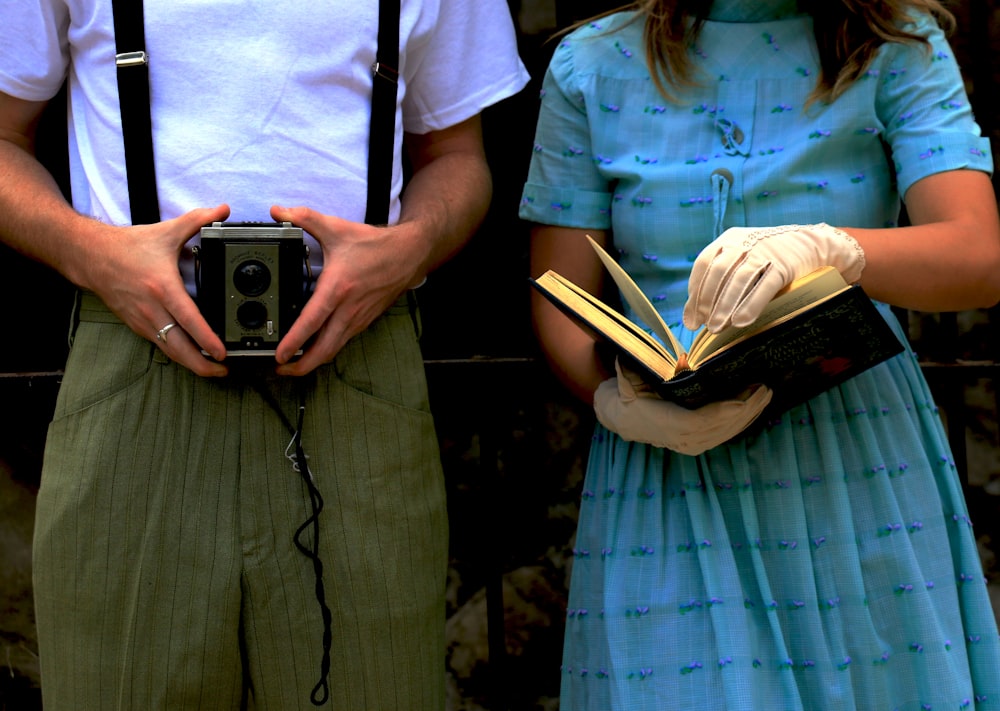 woman holding book while beside man holding vintage camera