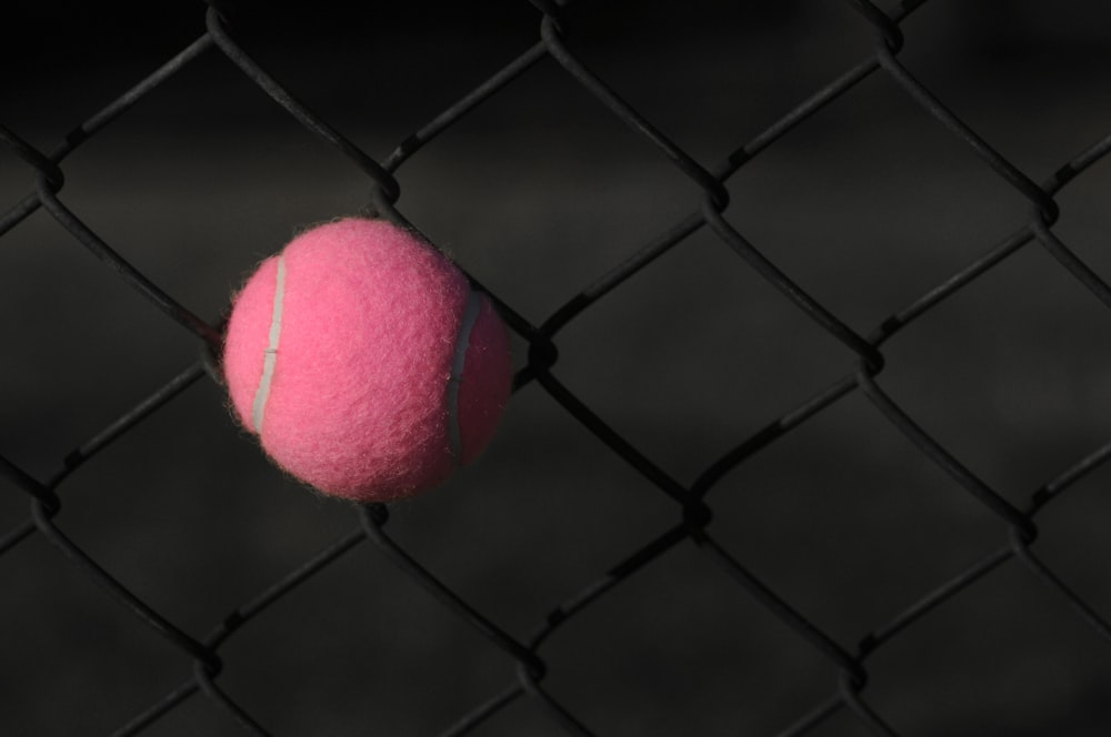 roter Tennisball auf grauem Stahlzaun
