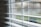 Horizontal blinds partially open with soft natural light filtering through. The focus is on the slats, while the background remains blurred giving a sense of depth.