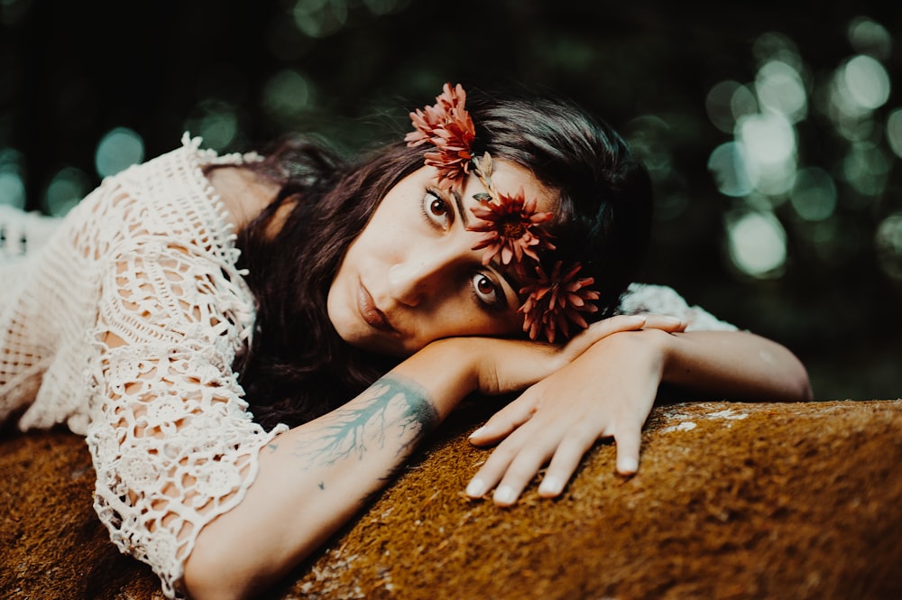 a woman with a flower in her hair leaning on a rock