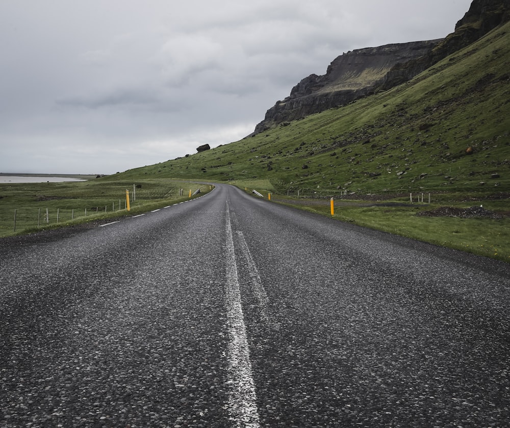 empty concrete road near mountain under cloudy sky at daytime