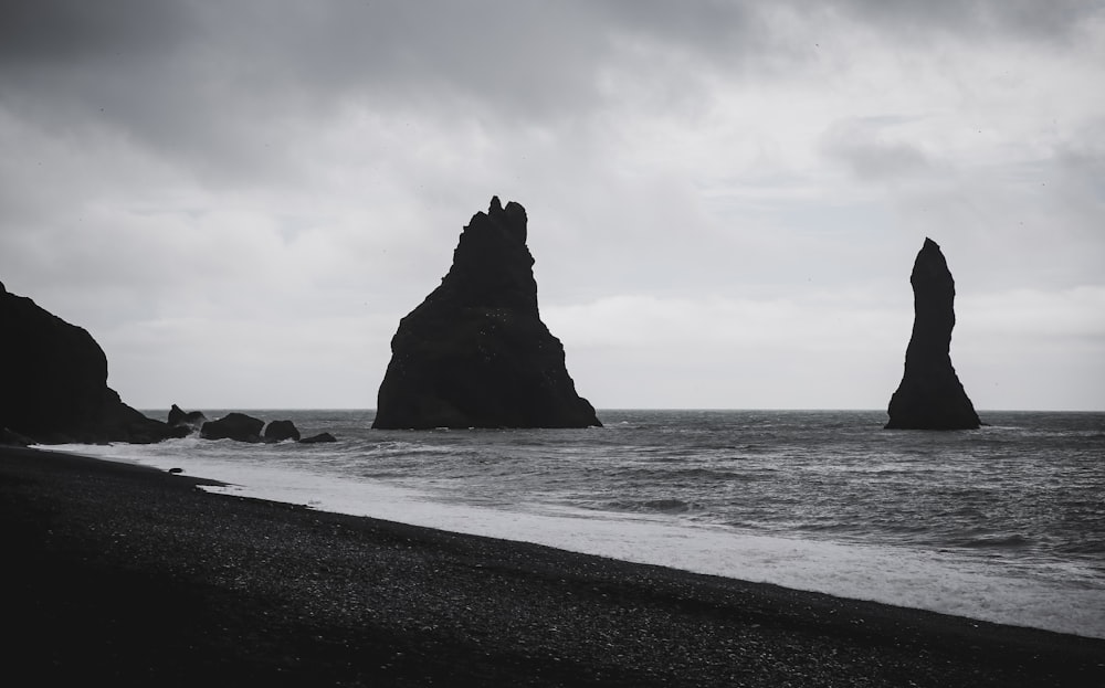 grayscale photography of rock formations on shore during daytime