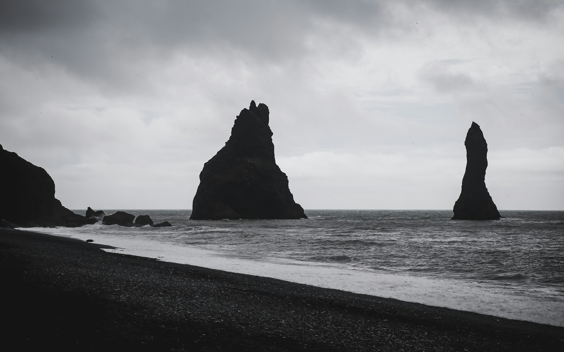 grayscale photography of rock formations on shore during daytime