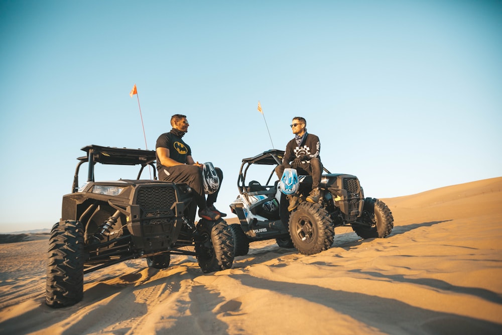 two men sitting on top of utility task vehicles on desert