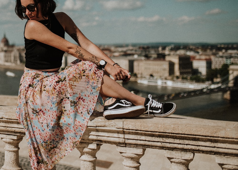 Frau in ärmellosem Oberteil, geblümtem Rock und schwarzen Vans Oldskool-Schuhen