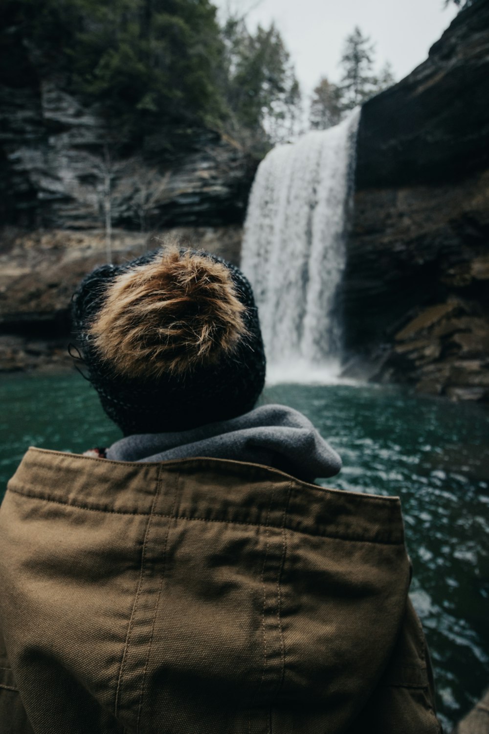 man wearing brown jacket in front of waterfalls