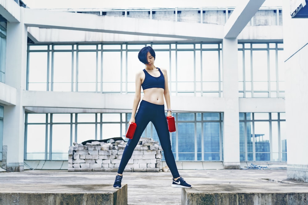 Frau trägt schwarzen Sport-BH und eine schwarze Hose, während sie zwei rote Gewichte hält
