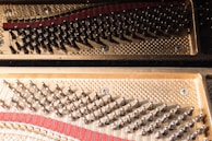 An intricate view of a piano's internal structure showcasing the tuning pins and the metallic strings. The gleaming metal components are arranged in an orderly fashion on a textured gold-colored surface.