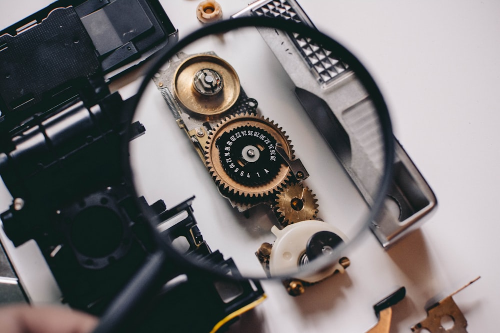 person using magnifying glass to see gold and white device gear