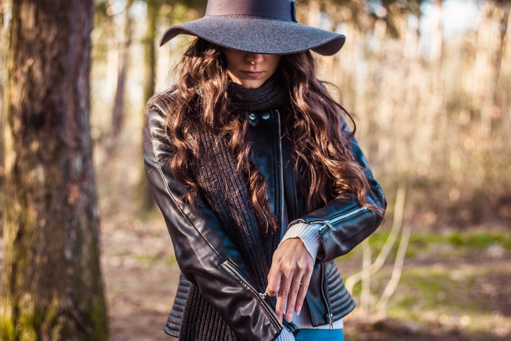 shallow focus photography of woman standing in front of tree while zipping her jacket