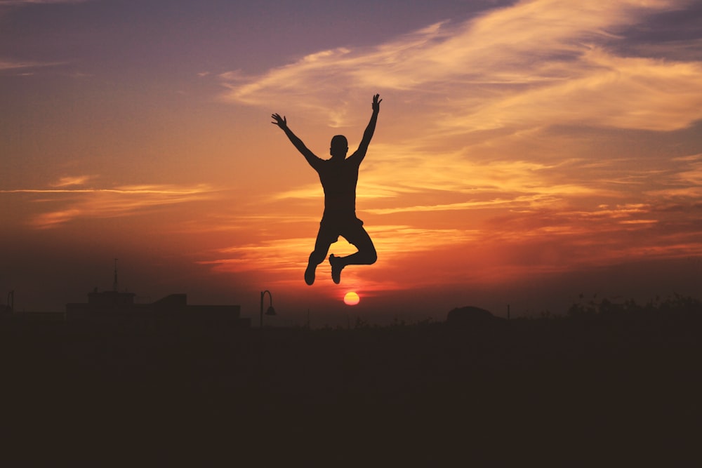 silhouette of man jumping raising both hands during golden hour