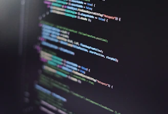 A close-up of a computer screen displaying lines of code in an integrated development environment. The code is colorful, with syntax highlighting for various programming elements such as keywords, strings, and functions. The text appears to be in a high-level programming language, possibly JavaScript or C#.