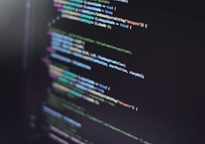 A close-up of a computer screen displaying lines of code in an integrated development environment. The code is colorful, with syntax highlighting for various programming elements such as keywords, strings, and functions. The text appears to be in a high-level programming language, possibly JavaScript or C#.