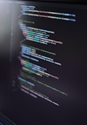 A close-up of a computer screen displaying lines of code in an integrated development environment. The code is colorful, with syntax highlighting for various programming elements such as keywords, strings, and functions. The text appears to be in a high-level programming language, possibly JavaScript or C#.