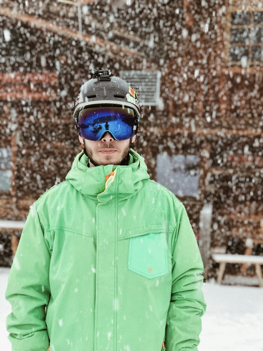 uomo in giacca con cappuccio con zip verde casco nero e occhiali neri in piedi sulla neve durante il giorno