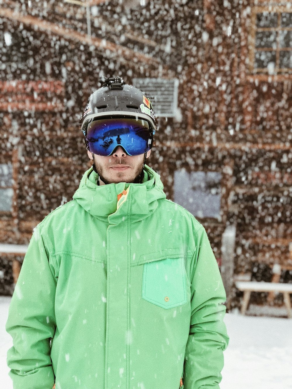 Hombre con chaqueta verde con capucha con cremallera, casco negro y gafas negras de pie sobre la nieve durante el día