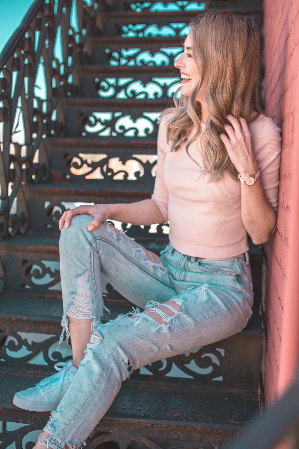 Frau in rosa halbärmeligem Oberteil und Used-Acid-Washed-Jeans sitzt auf der Treppe