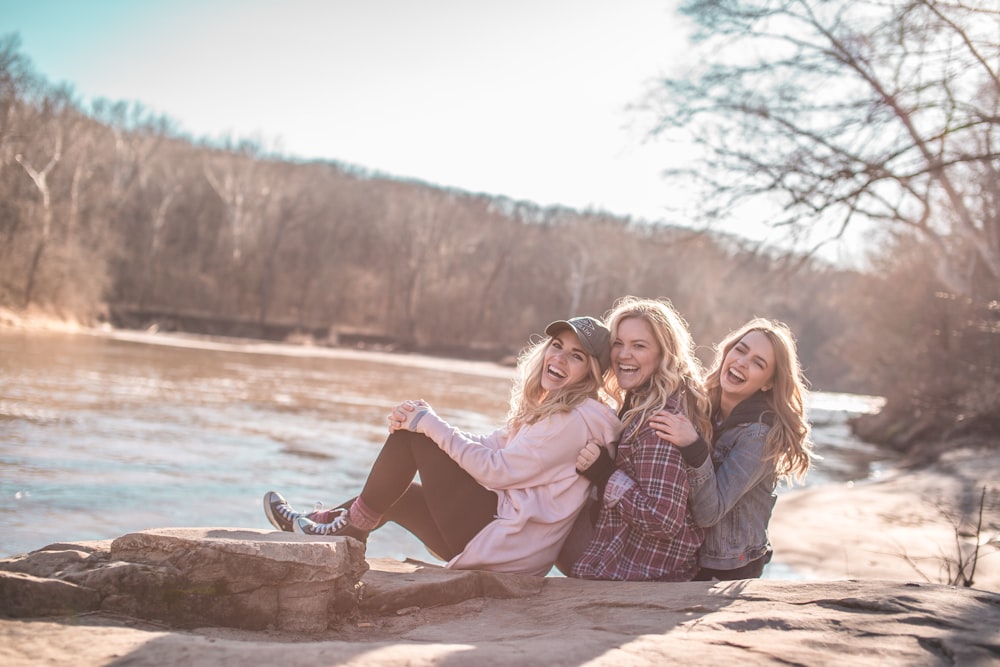 three women sitting on rock near body of water