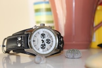 Elegant wristwatch displayed on a polished wooden table beside a seashell and a sunhat.