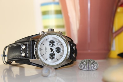 Elegant wristwatch displayed on a polished wooden table beside a seashell and a sunhat.