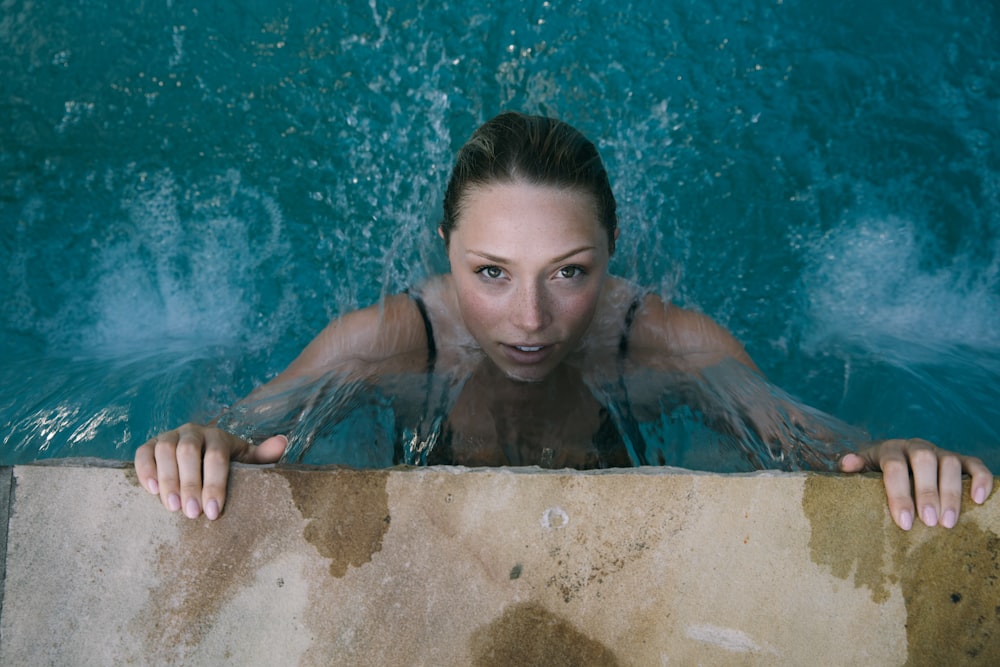 high-angle photo of woman in body of water holding on to brown concrete pavement