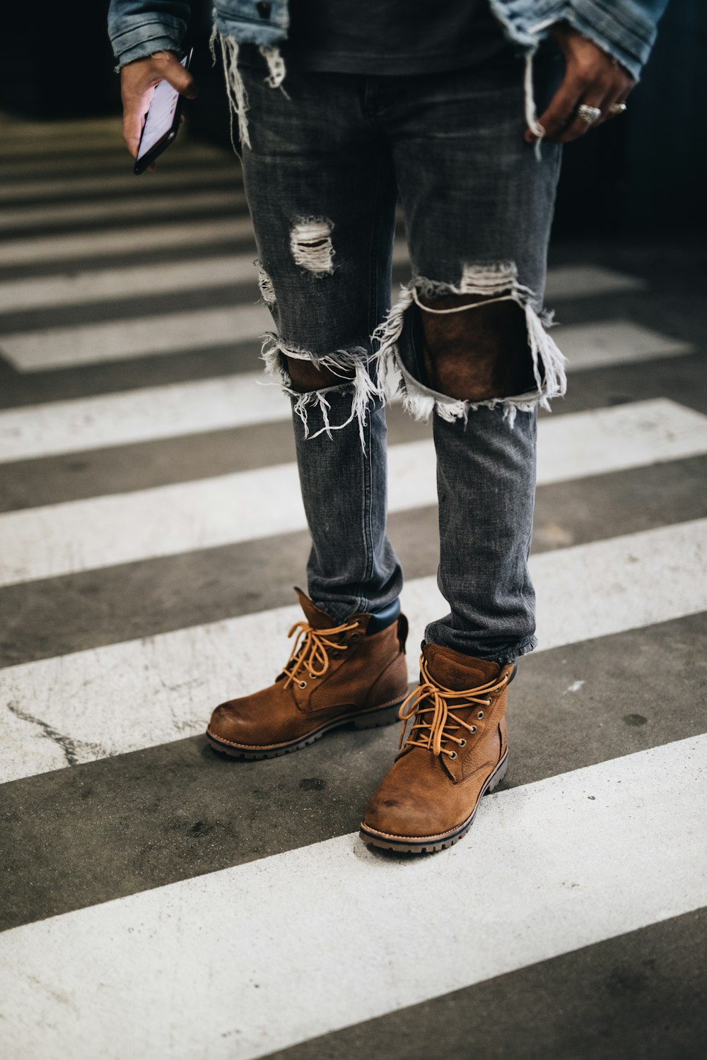 Person in abgenutzten grauen Denim-Jeans, die auf der Fußgängerlinie steht
