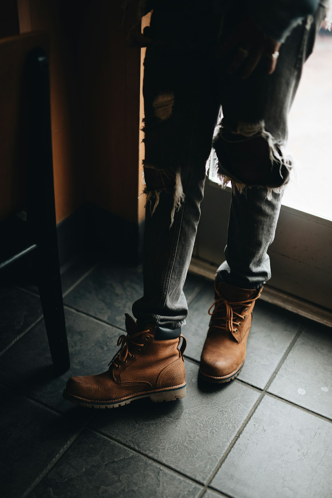 person wearing distressed blue denim jeans and pair of brown leather work boots beside glass door