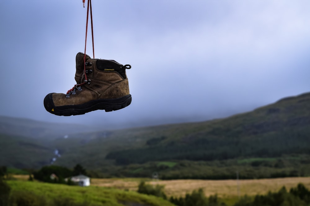 Braune und schwarze Stiefel hängen tagsüber mit Blick auf die Berge und das Feld