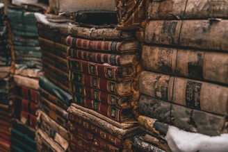 Stacks of old, weathered books are bound together, their covers worn and colors faded. The books show signs of age with frayed edges and dusty surfaces, evoking a sense of history and timelessness.