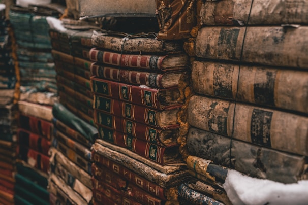 Stacks of old, weathered books are bound together, their covers worn and colors faded. The books show signs of age with frayed edges and dusty surfaces, evoking a sense of history and timelessness.