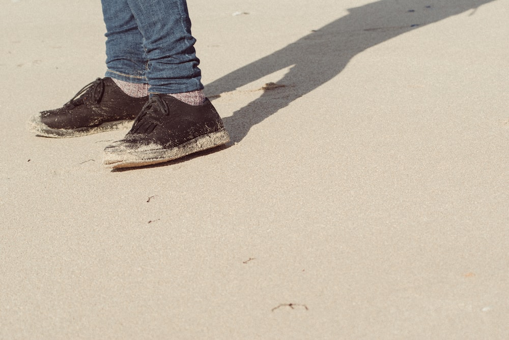 person wearing black-and-white low-top sneakers on sand