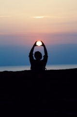 silhouette of person with both hands over his head tracing the sun during golden hour photography