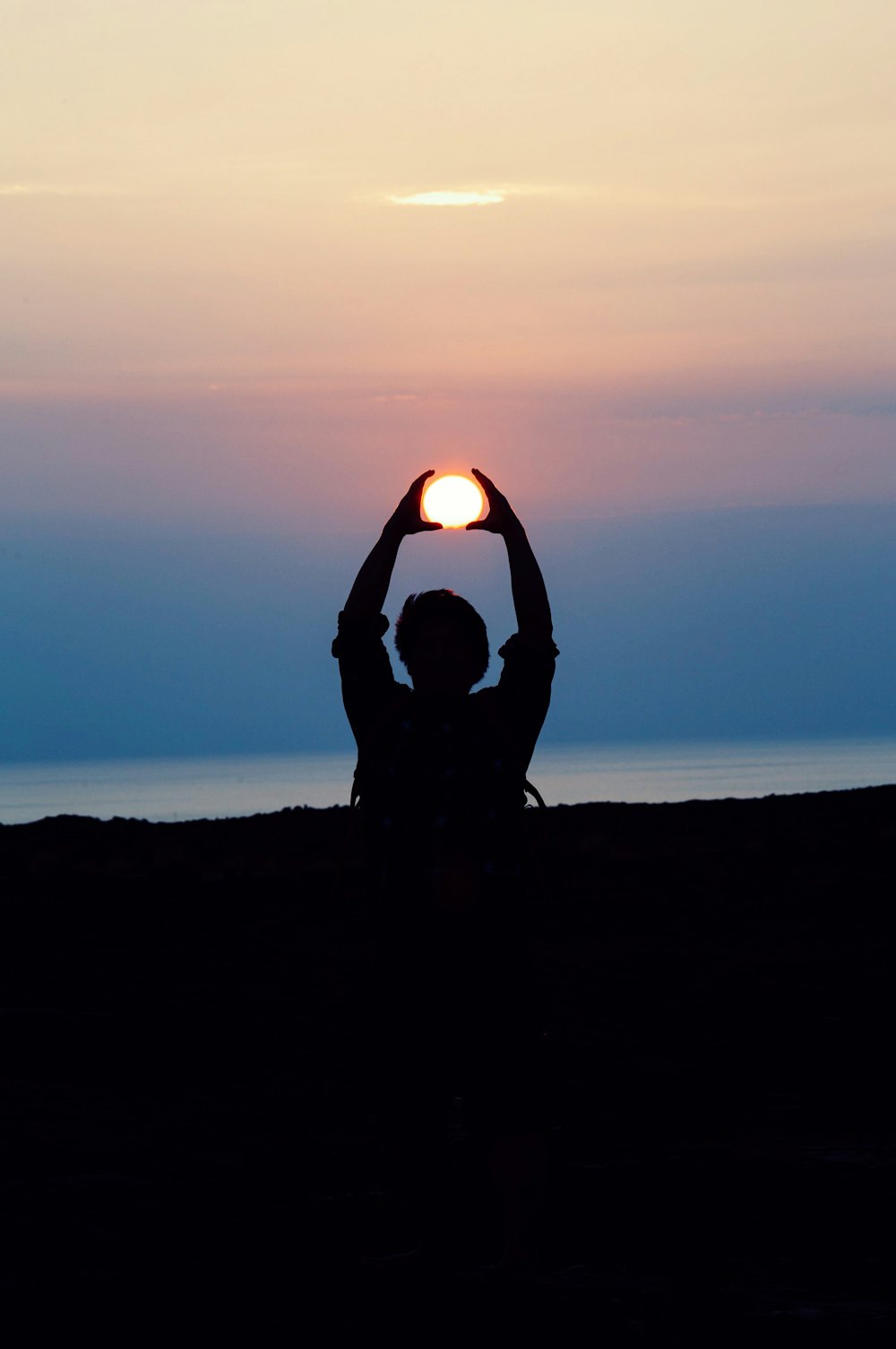 Silhouette einer Person mit beiden Händen über dem Kopf, die die Sonne während der Fotografie zur goldenen Stunde nachzeichnet