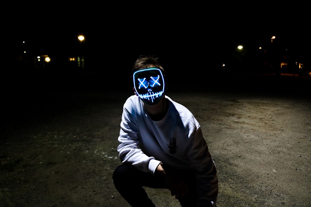 man wearing black and white purge mask and white crew-neck sweatshirt while kneeling left knee