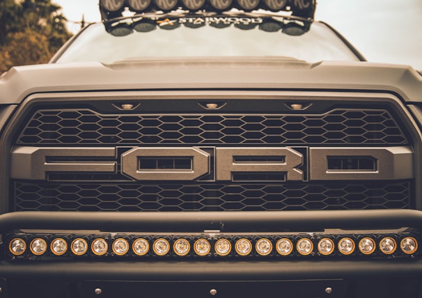 A close-up of a 2019 Ford F-150’s front grille with the Texas flag waving in the background.