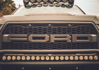 Close-up view of the front grille of a Ford vehicle, showcasing its bold design and prominent logo. The image highlights a row of circular lights mounted below the grille.