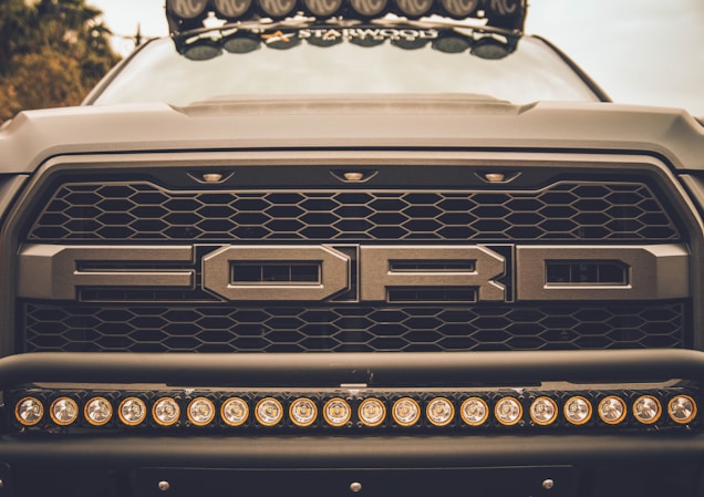 Close-up view of the front grille of a Ford vehicle, showcasing its bold design and prominent logo. The image highlights a row of circular lights mounted below the grille.