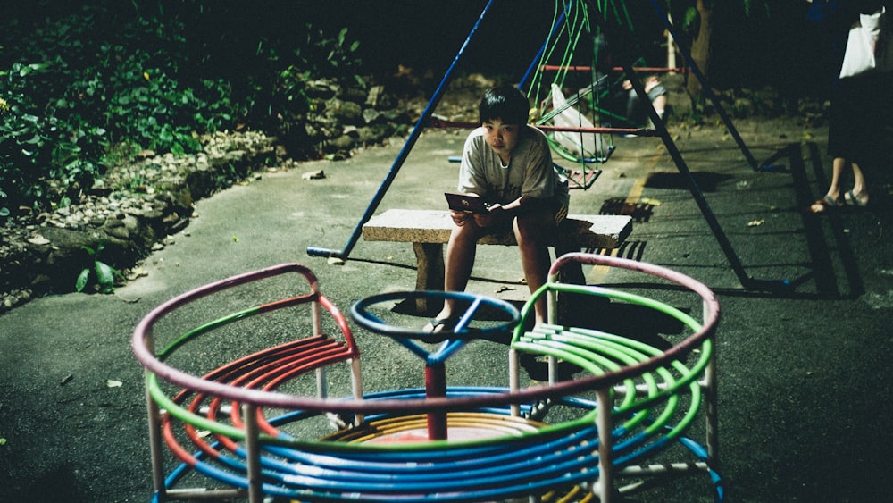 boy sitting on concrete bench while holding laptop