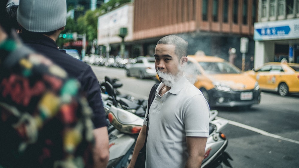 selective focus photography of man standing beside road while smoking